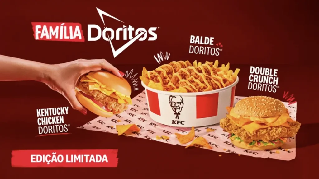Uma imagem publicitária com um fundo vermelho escuro promocionando a "Família Doritos" do KFC. No centro, uma mão está segurando um sanduíche "Kentucky Chicken Doritos", que parece ser um filé de frango frito com queijo e alguns Doritos visíveis. Ao lado, há um balde grande de batatas fritas do KFC, generosamente cobertas com queijo e pedaços de Doritos, identificado como "Balde Doritos". À direita, um segundo sanduíche, chamado "Double Crunch Doritos", é exibido em um invólucro de papel do KFC. Alguns Doritos soltos estão espalhados na base da imagem. No canto inferior esquerdo, há um selo vermelho com a inscrição "EDIÇÃO LIMITADA". O logotipo do KFC é proeminente no balde de batatas e no papel do sanduíche.