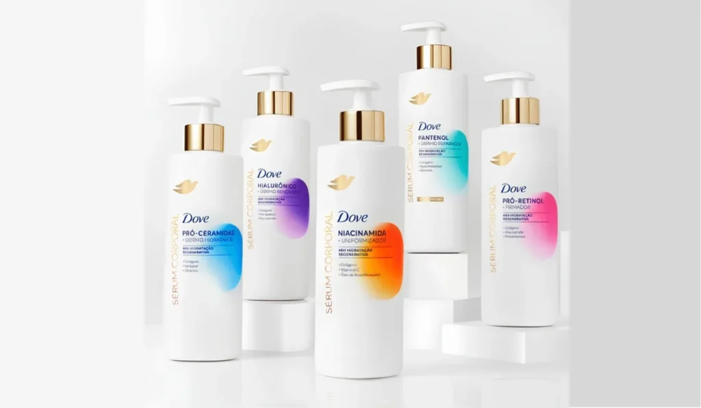 Uma fileira de cinco frascos brancos de Sérum Corporal Dove com tampas douradas. Cada frasco tem um rótulo com um ingrediente principal diferente e um gradiente de cor vibrante. Da esquerda para a direita, os rótulos são: "PRÓ-CERAMIDAS" com gradiente azul, "HIALURÔNICO" com gradiente roxo, "NIACINAMIDA" com gradiente laranja-avermelhado, "PANTENOL" com gradiente ciano e "PRÓ-RETINOL" com gradiente rosa.