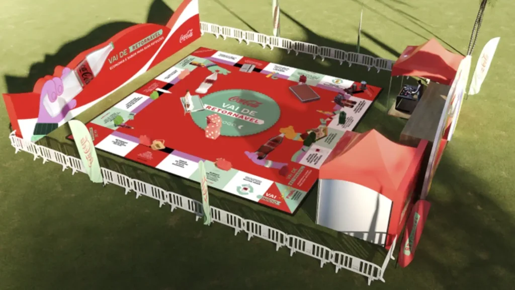 Uma grande representação de um jogo de tabuleiro em tamanho real, com as cores vermelho, branco e verde-claro. O tabuleiro está em uma área gramada e é cercado por uma cerca branca baixa. No centro do tabuleiro, há um círculo verde com o texto "Coca-Cola Vai de Retornável" e uma representação de dados. Várias peças do jogo, em formato de garrafas e outros objetos, estão espalhadas pelas casas do tabuleiro. Ao redor do tabuleiro, há estruturas de marca da Coca-Cola em vermelho e branco, e duas tendas vermelhas, uma delas com equipamentos de DJ. Uma bandeira branca com o logo da Coca-Cola também é visível.