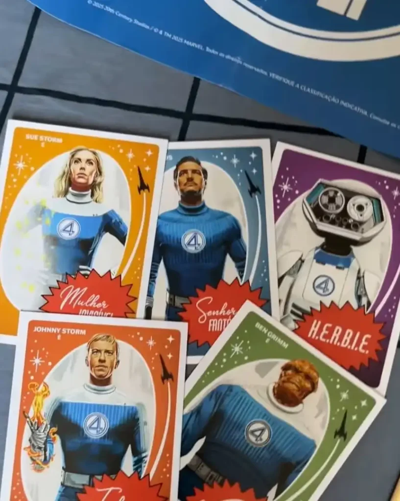 Uma imagem detalhada mostra cinco cartões promocionais do Quarteto Fantástico dispostos sobre uma superfície quadriculada azul. Cada cartão apresenta um personagem diferente em um estilo de arte que lembra pôsteres vintage ou capas de quadrinhos, com o logotipo do "4" no centro do peito de cada personagem.