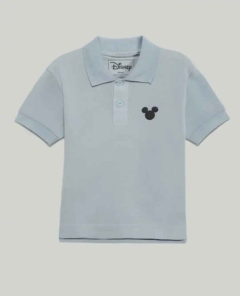 Uma camisa polo infantil azul clara com o logotipo do Mickey Mouse em preto no lado esquerdo do peito. A gola e as mangas curtas são do mesmo tom de azul. Há três botões azuis claros na carcela do colarinho. A etiqueta da marca Disney é visível no interior da gola. A camisa está sobre um fundo cinza claro.