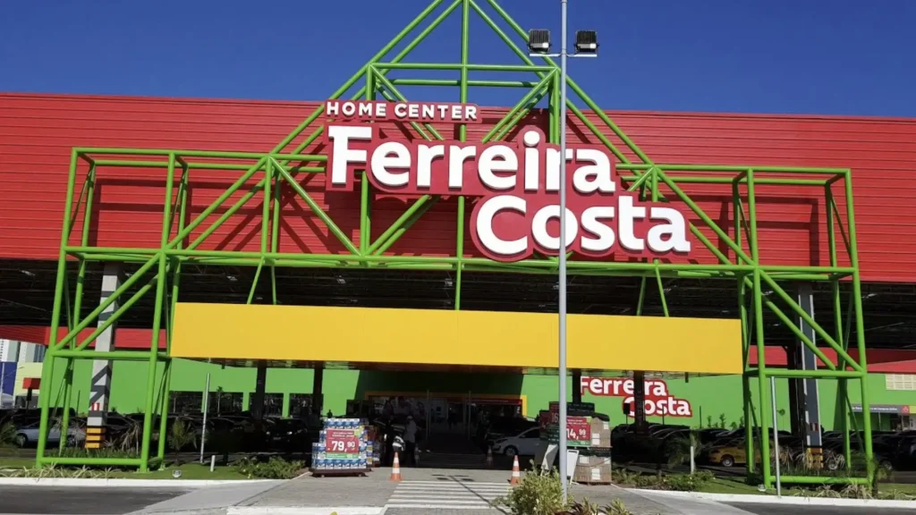 Fachada da loja Ferreira Costa Home Center, destacando sua arquitetura moderna com treliças verdes, painel amarelo e o logotipo da empresa sob um céu azul.