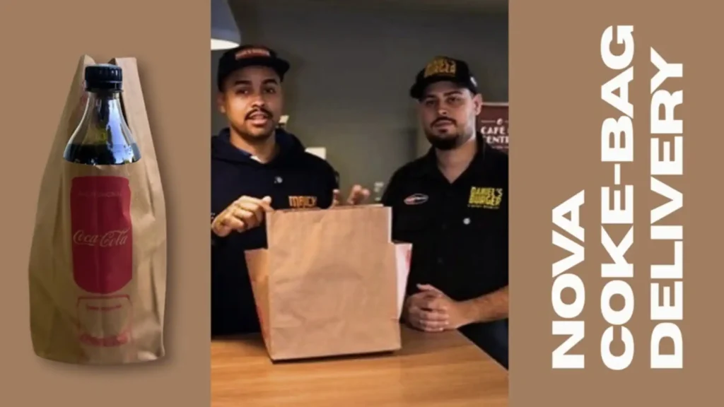 Uma colagem de três partes mostra um vídeo em andamento e uma imagem de um produto. À esquerda, uma sacola de papel parda com uma garrafa de Coca-Cola dentro. A sacola tem o formato da garrafa de Coca-Cola impressa em vermelho e branco, e um copo embaixo da garrafa também em branco e vermelho. No centro, dois homens com bonés de beisebol estão em pé atrás de um balcão de madeira, olhando para a câmera e segurando uma sacola de papel parda aberta. O homem da esquerda tem um bigode e barba e está vestindo um moletom azul escuro com um logotipo branco. O homem da direita tem um bigode e uma barba rala e está vestindo uma camisa polo preta com um logotipo branco. Ao fundo, um interior de restaurante escuro com uma placa branca. À direita, uma grande faixa vertical marrom-clara tem as palavras "NOVA COKE-BAG DELIVERY" em branco.