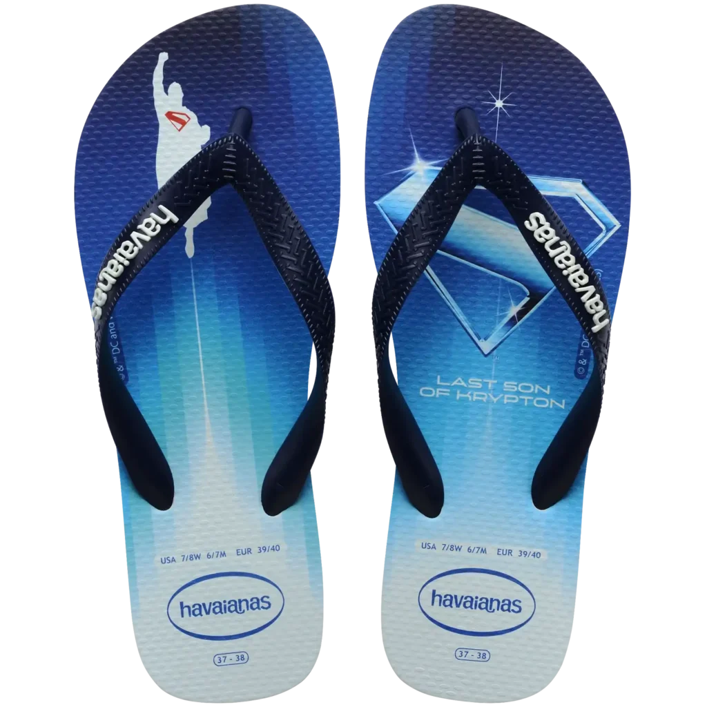 Chinelo Havaianas azul com estampa inspirada no Superman. O pé esquerdo traz a silhueta do herói voando com o símbolo "S" em vermelho no peito, enquanto o pé direito exibe o clássico escudo do Superman em azul com brilho, acompanhado da frase "Last Son of Krypton" ("Último Filho de Krypton"). As tiras são pretas com o logo "havaianas" em branco. Numeração 37-38 (USA 7/8W, 6/7M | EUR 39/40).