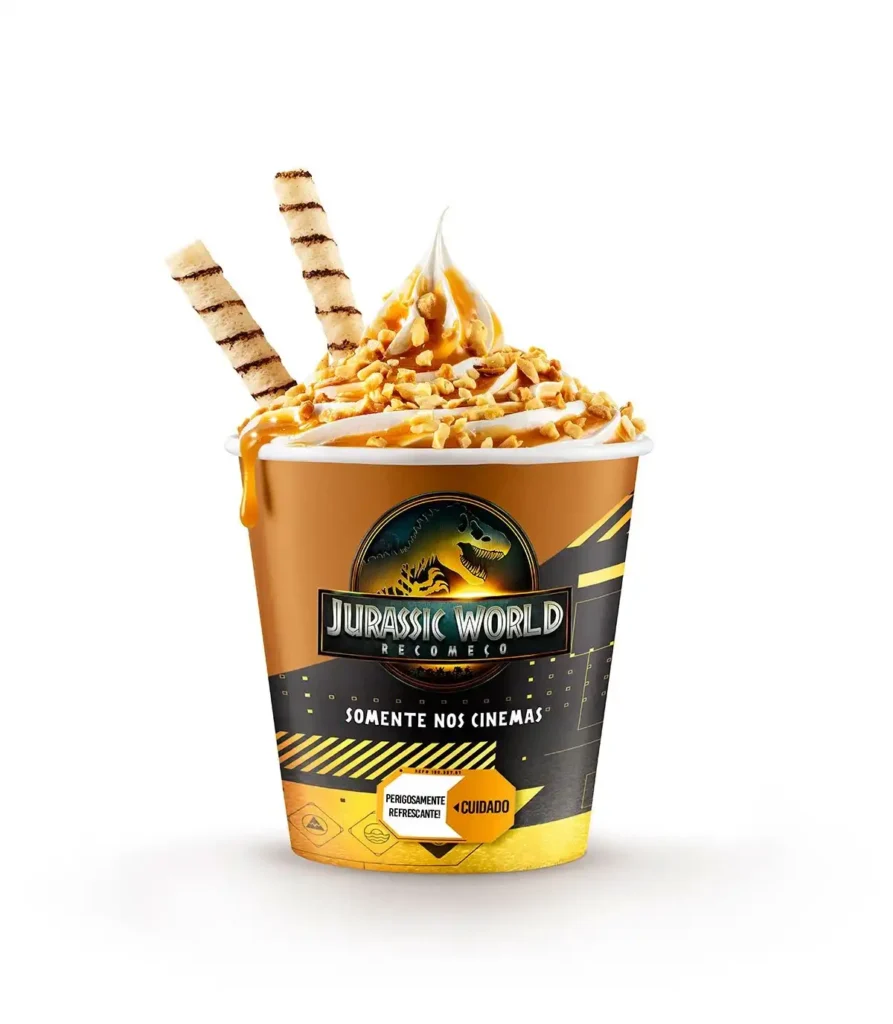 Um sundae em um copo temático de "Jurassic World: Recomeço" da Bobs, com sorvete de massa branca, calda de caramelo, amendoins picados e dois canudos de waffer.