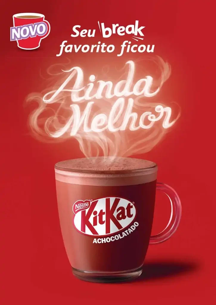 Um copo transparente cheio de chocolate quente espumoso com um logotipo vermelho "Kit Kat" impresso no copo. O chocolate quente tem um tom marrom escuro e a espuma é mais clara. Vapor branco sobe do copo e forma as palavras "Ainda Melhor" em letras cursivas e brilhantes. No canto superior esquerdo, há um logotipo vermelho "NOVO" em um círculo branco. Acima do vapor, o texto em português diz "Seu break favorito ficou". O fundo é vermelho.