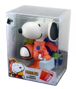 Snoopy em traje de astronauta laranja, segurando uma mala azul clara, dentro de uma embalagem de acrílico.