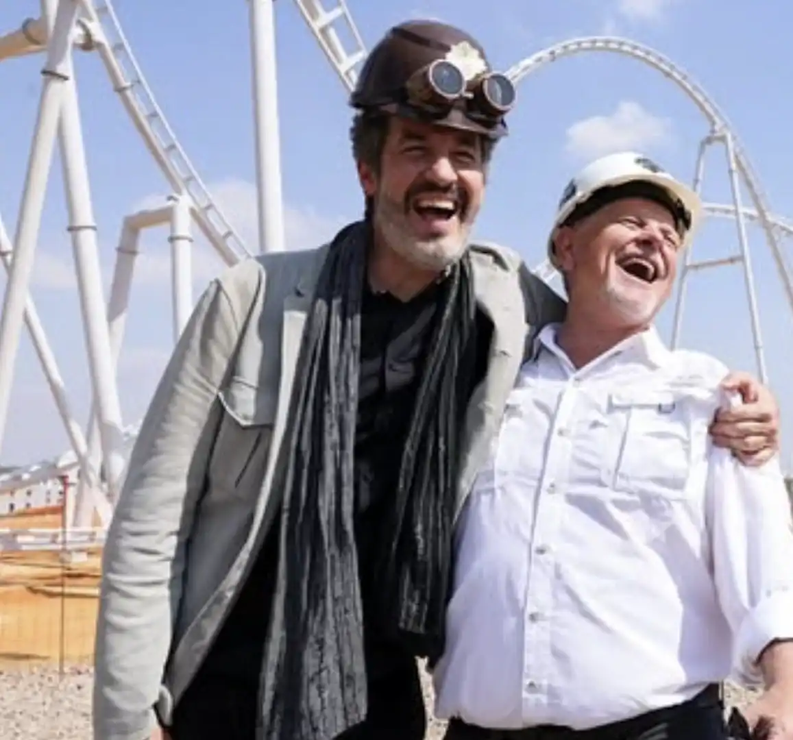 Foto de duas pessoas, sendo uma aparentemente o dono do Cacau Show, Alexandere Costa, e um engenheiro, rindo em frente à montanha-russa do Cacau Park em construção.
