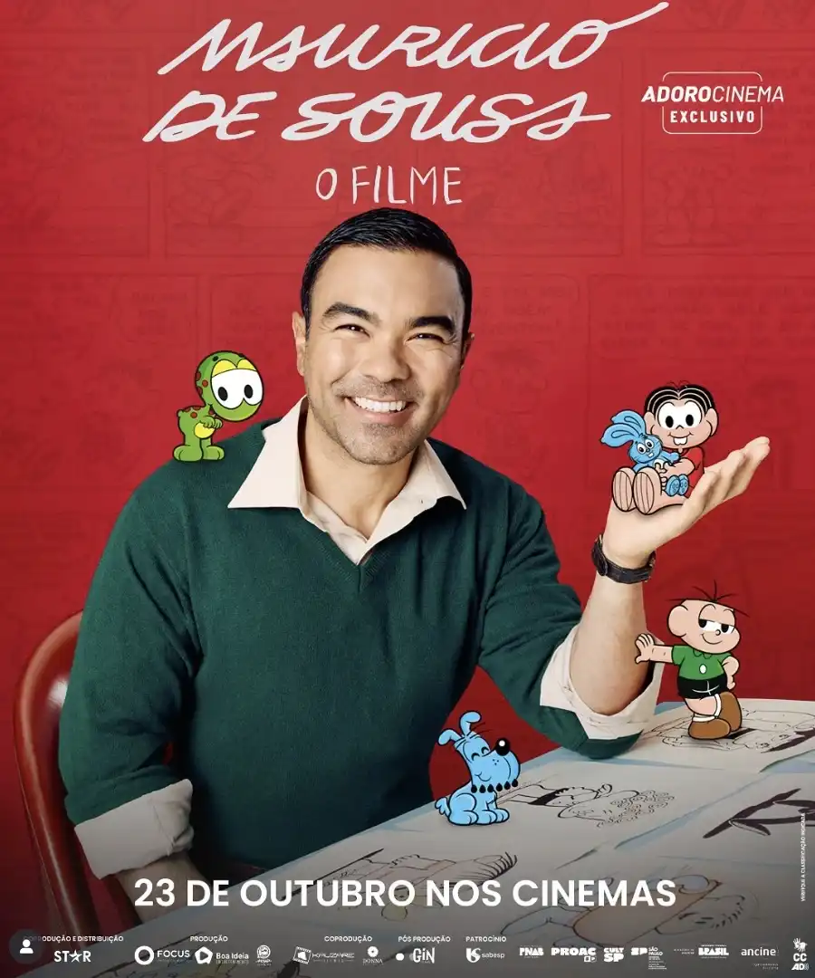 Um homem sorridente com uma camisa polo bege e um suéter verde escuro está posando com personagens da Turma da Mônica. Na sua mão esquerda, ele segura um boneco de pelúcia do Sansão, o coelho azul da Mônica, enquanto um Cebolinha em miniatura aponta para ele. No ombro direito do homem, está um boneco do dinossauro Horácio. O fundo é vermelho com ilustrações de quadrinhos da Turma da Mônica.