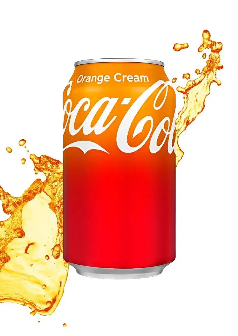 Uma lata de Coca-Cola de cor laranja no topo, mudando para vermelho na parte inferior. O logotipo "Coca-Cola" é branco, e "Orange Cream" está escrito em branco na parte superior. Há um respingo de líquido laranja efervescente em ambos os lados da lata, com um fundo branco puro.