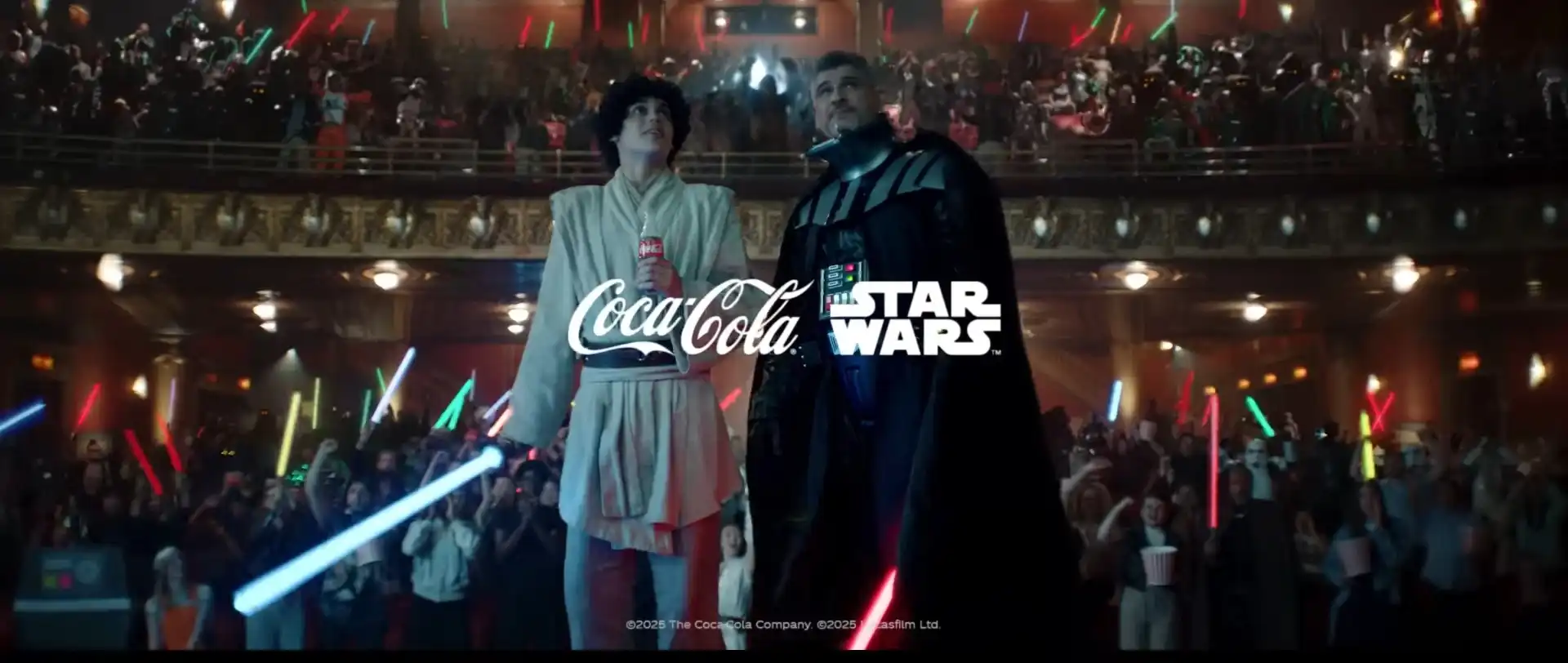 Imagem de divulgação da parceria entre Coca-Cola e Star Wars, mostrando um jovem em traje de Jedi e Darth Vader juntos em um teatro lotado.