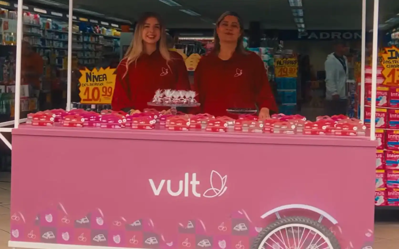 Foto de duas promotoras da marca Vult em um carrinho rosa dentro de um supermercado.