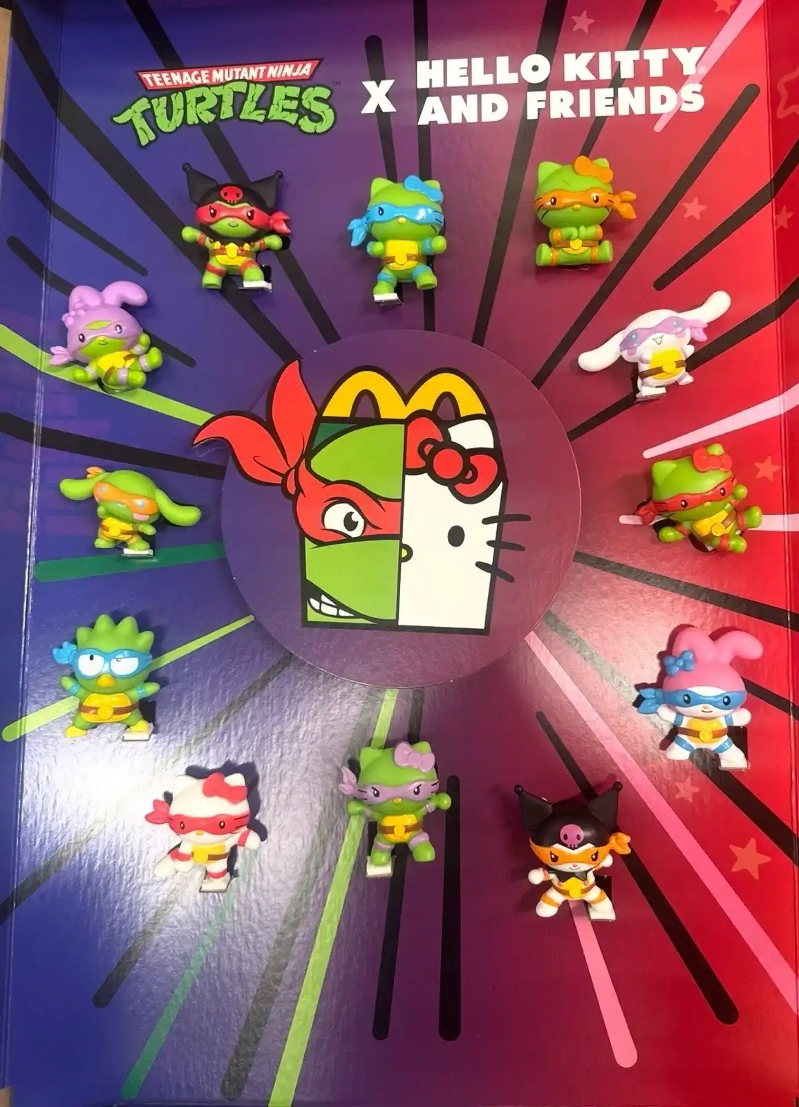 Um display de colecionáveis do McDonald's mostrando o crossover "Hello Kitty and Friends X Teenage Mutant Ninja Turtles", com 12 figuras de personagens das duas franquias trocando de roupas.