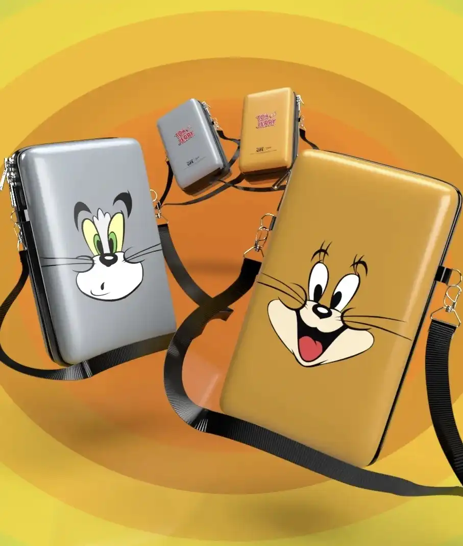 Quatro bolsas pequenas e colecionáveis de Tom e Jerry. Duas bolsas maiores, cinza com o rosto de Tom e marrom com o rosto de Jerry, estão na frente, enquanto duas menores estão mais atrás. O fundo é de anéis concêntricos laranjas e amarelos.