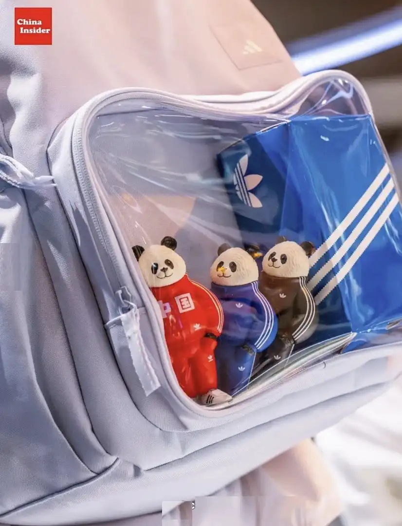 Três miniaturas de pandas vestindo agasalhos Adidas em um bolso de mochila transparente.