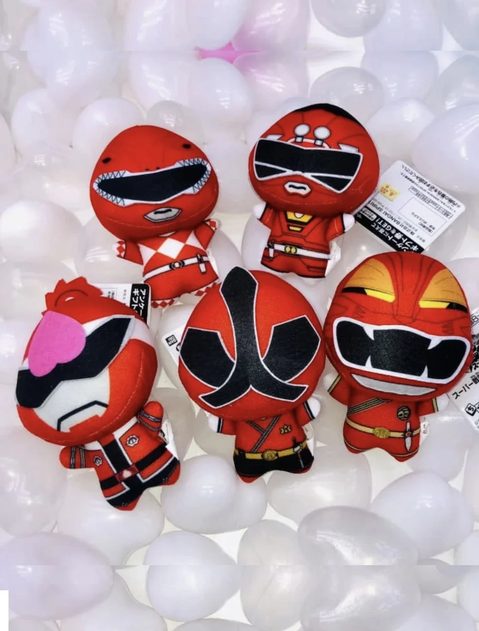 Cinco pelúcias de personagens vermelhos de Super Sentai, incluindo o de Zenkaiger, Donbrothers, King-Ohger, Ryusoulger e Gokaiger. Os bonecos têm design de chibi, com corpos pequenos e cabeças grandes, e estão dispostos sobre um fundo branco.