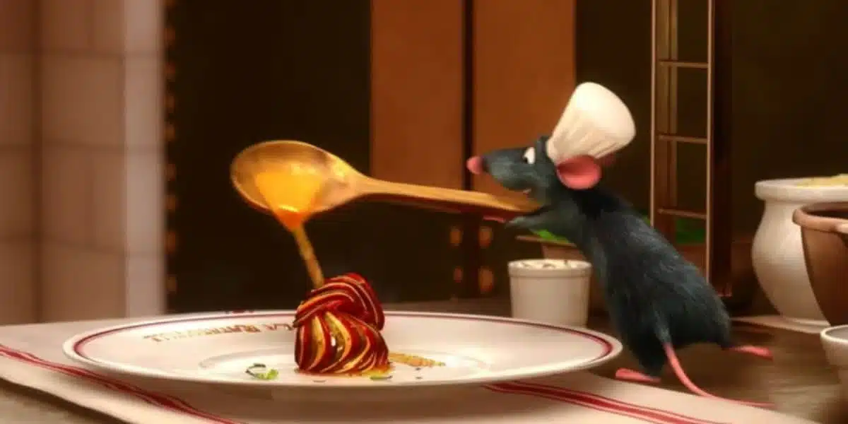 O rato Remy, usando um chapéu de chef, está derramando um molho dourado sobre um prato de ratatouille elegantemente arrumado.