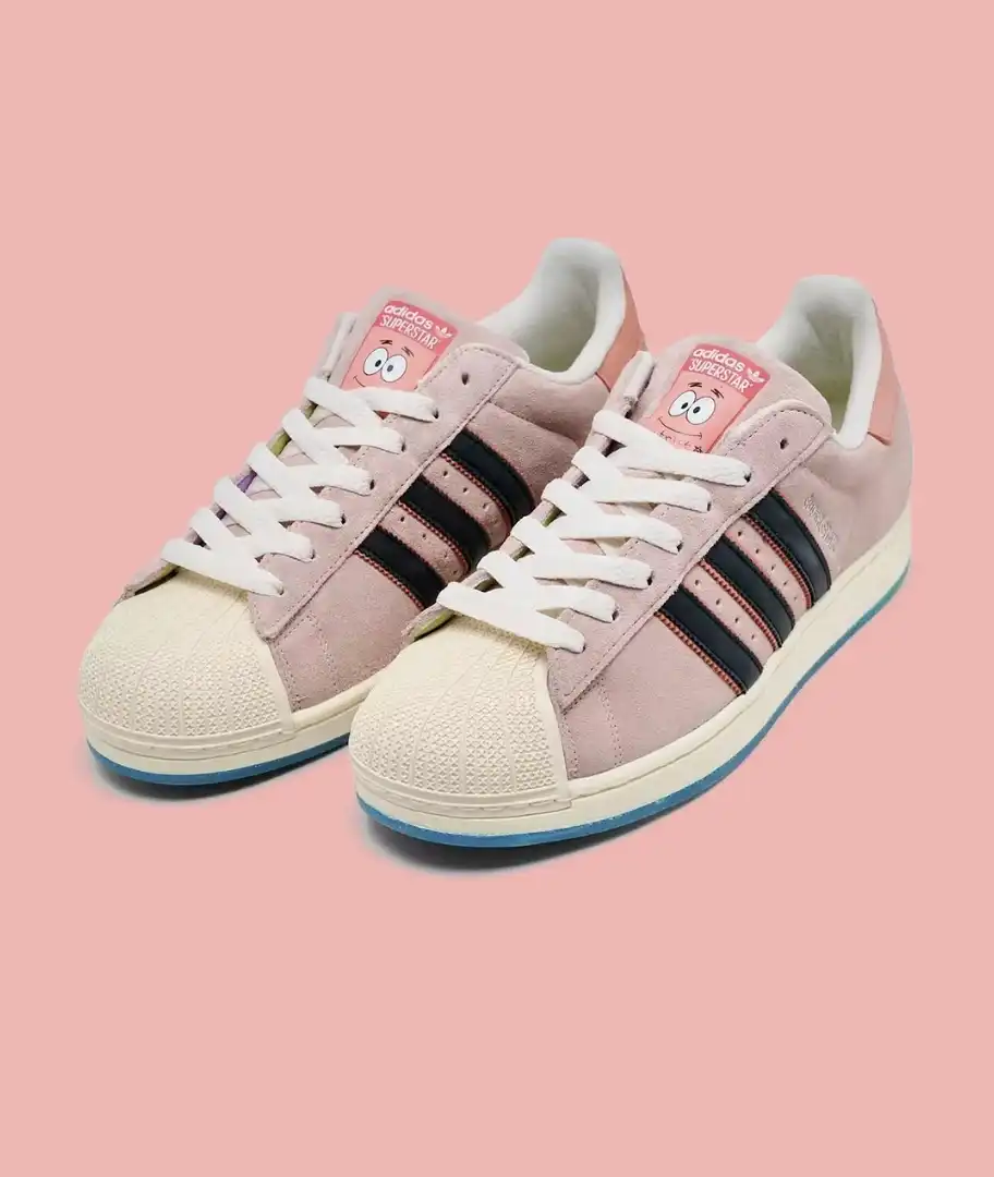 Um par de tênis adidas Superstar em colaboração com o desenho Bob Esponja. Os tênis são rosa, com três listras pretas e o rosto do Patrick Estrela na língua.