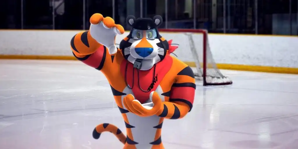 Quatro representações do Tigre Tony, mascote dos Sucrilhos Kellogg's, exibindo sua evolução visual ao longo do tempo. Da esquerda para a direita: a primeira imagem mostra uma versão mais antiga, com traços menos definidos e um lenço vermelho no pescoço. A segunda imagem é uma ilustração animada, com o tigre sorrindo e o mesmo lenço. A terceira e quarta imagens mostram versões mais modernas do personagem, com a quarta sendo a mais atual, onde o Tigre Tony aparece mais musculoso, com um polegar para cima e um sorriso confiante, sempre usando seu lenço vermelho característico.
