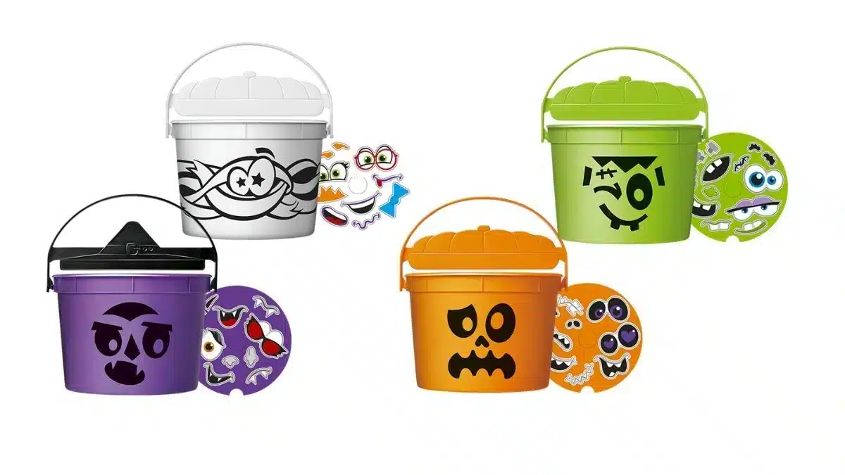 A imagem mostra quatro baldes de Halloween do McDonald's, cada um em uma cor e com um personagem diferente: um balde branco de fantasma, um balde laranja de abóbora, um balde verde de Frankenstein e um balde roxo de vampiro. Ao lado de cada balde há um conjunto de adesivos para personalização.