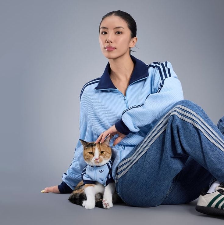 Uma mulher e seu gato deitados no chão, ambos usando agasalhos Adidas azuis.