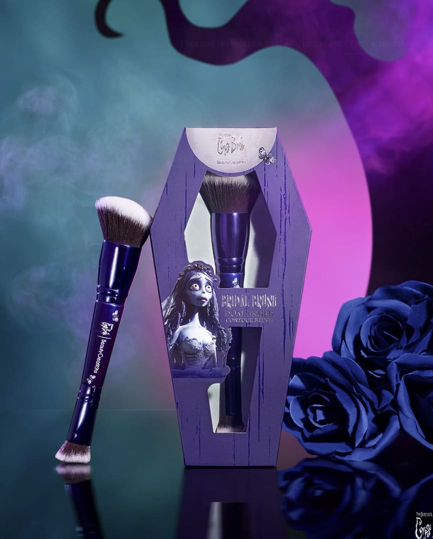 Pincel de maquiagem da coleção Beauty Creations A Noiva-Cadáver, com cabo roxo, ao lado da embalagem em formato de caixão.