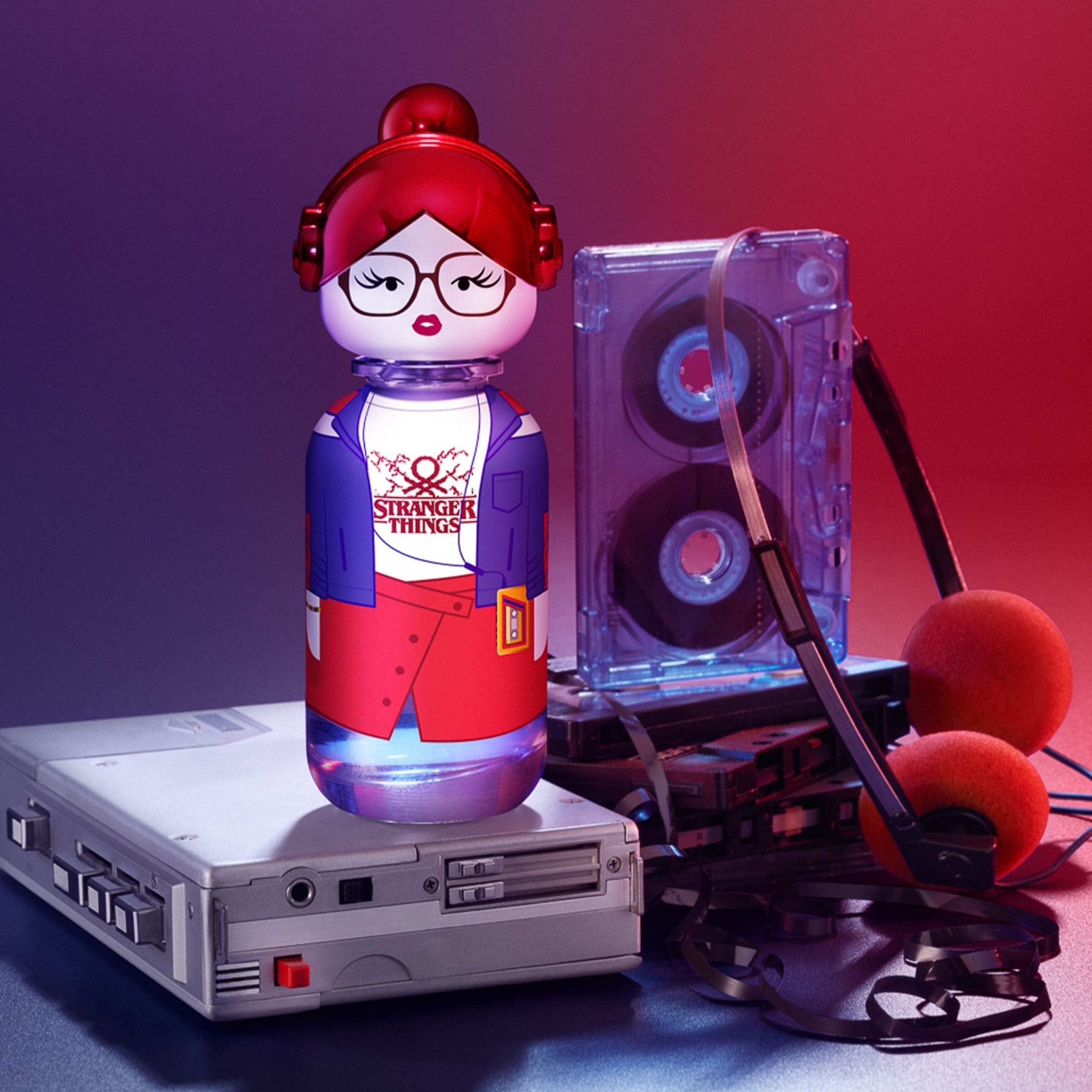 Frasco de perfume Benetton "Stranger Things" em formato de boneca com fones de ouvido, sobre um walkman vintage, com uma fita cassete e fones de ouvido retrô ao lado.
