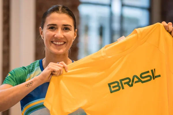 Atleta sorrindo segurando uma camisa amarela do Brasil.