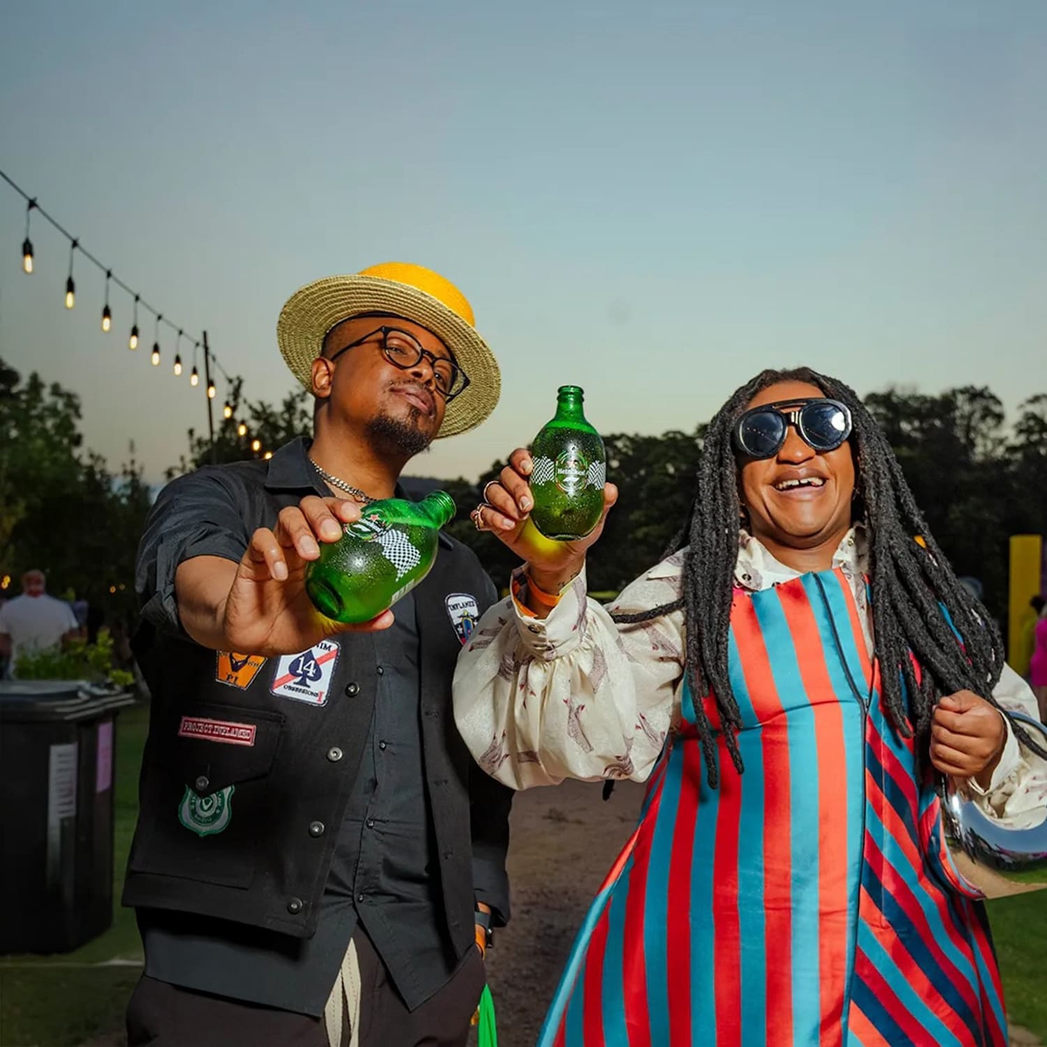 Duas pessoas segurando as garrafas Heineken de design Fórmula 1 em um evento ao ar livre.