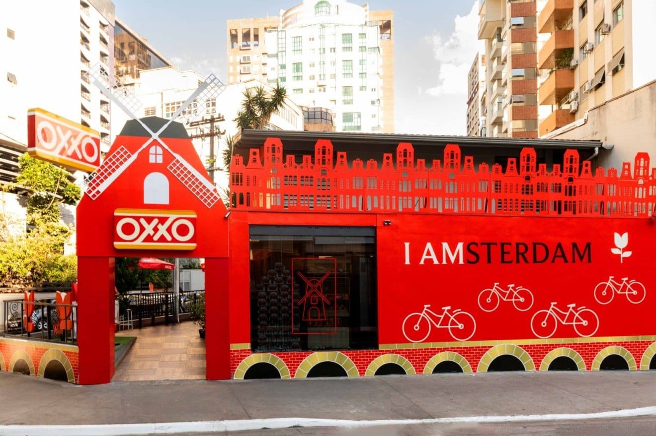 Fachada de loja Oxxo com tema da cidade de Amsterdã, moinho de vento, bicicletas e a frase "I AMSTERDAM".
