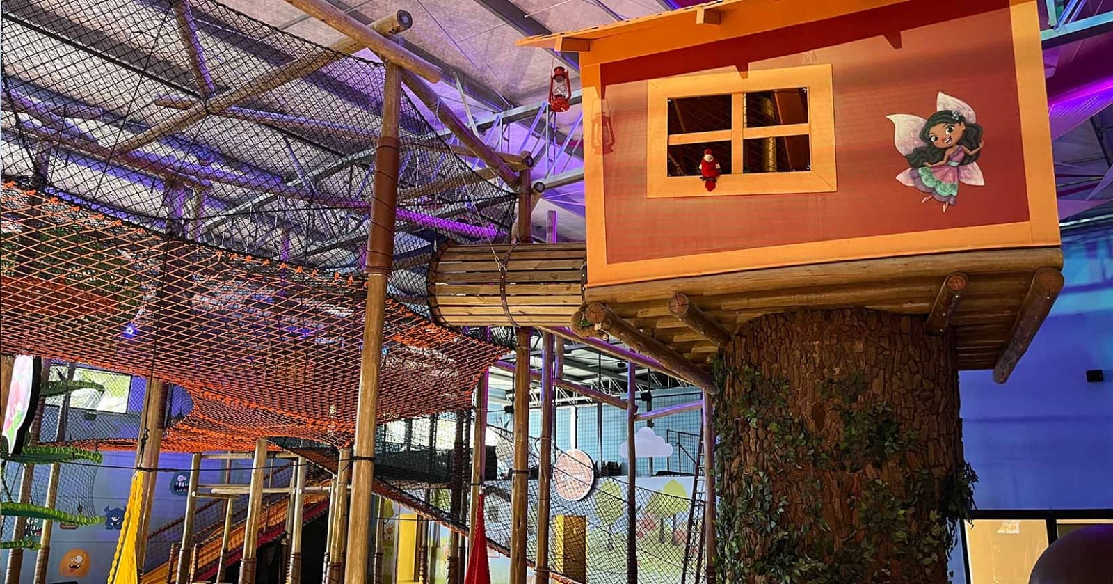 Casa na árvore colorida em um playground indoor com rede de escalada e detalhes em madeira.