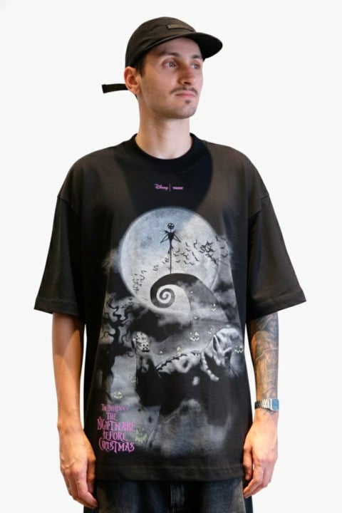 Um homem vestindo uma camiseta preta com estampa de Jack Skellington no topo de uma colina espiralada contra a lua cheia, da coleção "O Estranho Mundo de Jack".