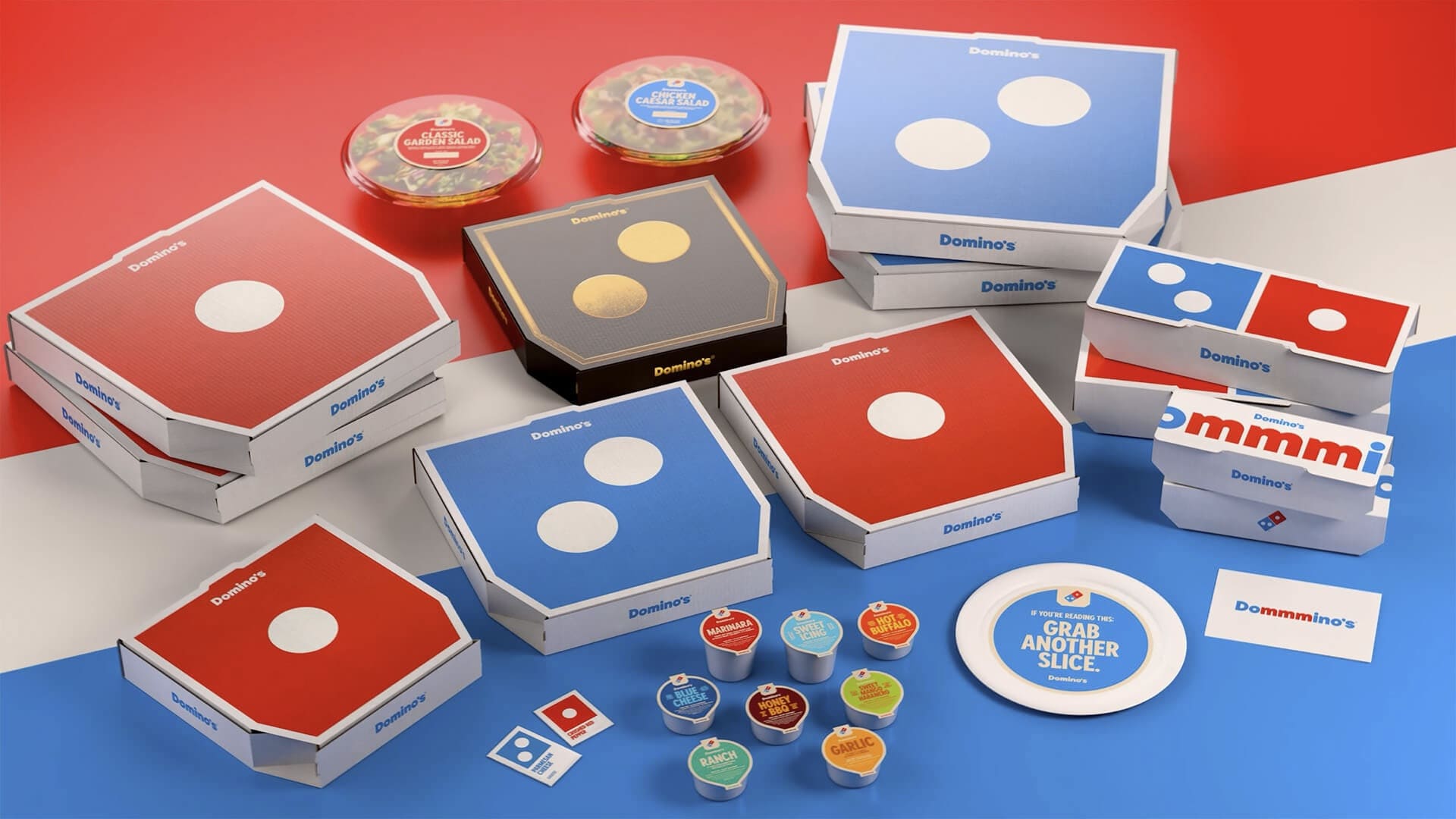Variedade de embalagens da Domino's, incluindo caixas de pizza vermelhas e azuis com o logo de dominó, saladas, caixas menores pretas e molhos, dispostas sobre um fundo branco, vermelho e azul.