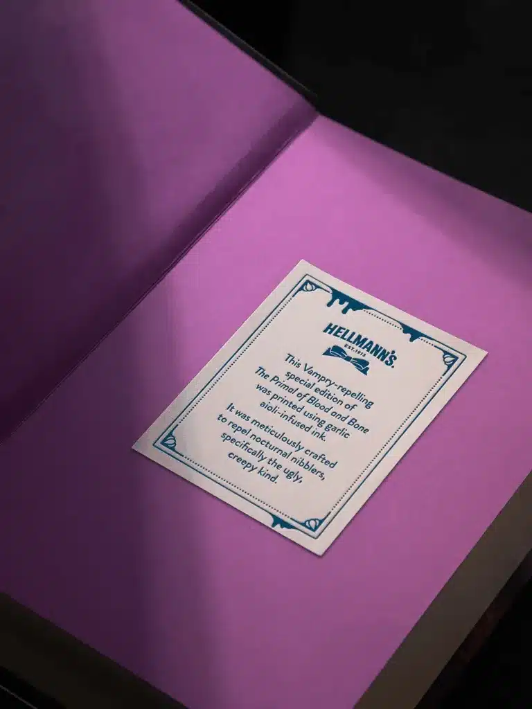 Uma etiqueta branca em um livro roxo escuro, detalhando que a edição especial foi impressa com tinta infundida com alho para repelir vampiros.