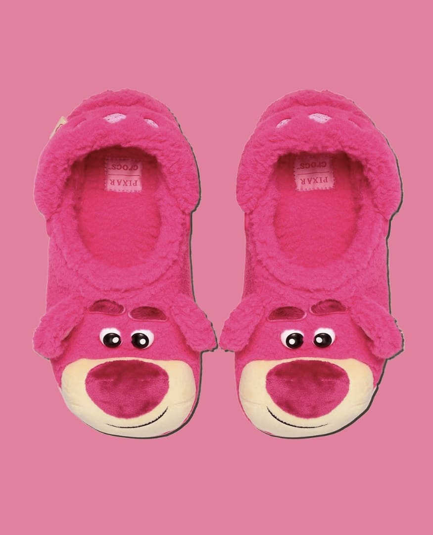 Um par de chinelos Crocs rosa totalmente forrado de pelúcia, com o formato da cabeça do urso Lotso de Toy Story 3.