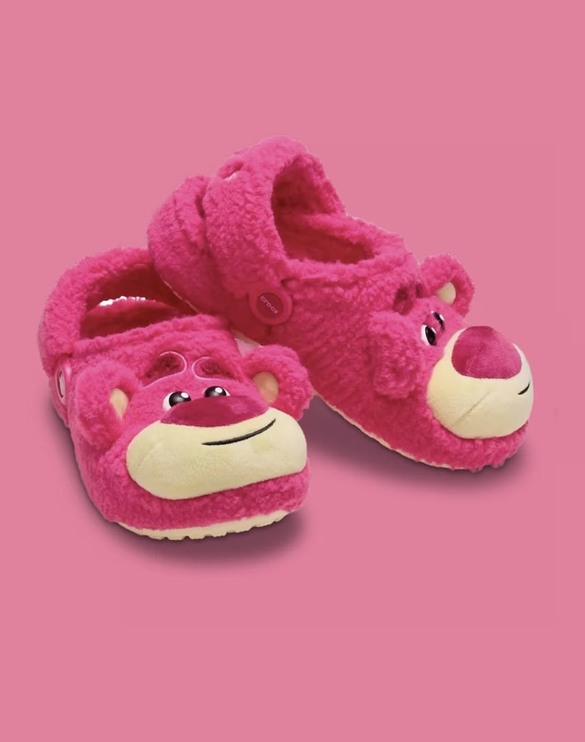 Um par de Crocs felpudos rosa, modelados como o urso Lotso de Toy Story 3, apresentados em um ângulo.