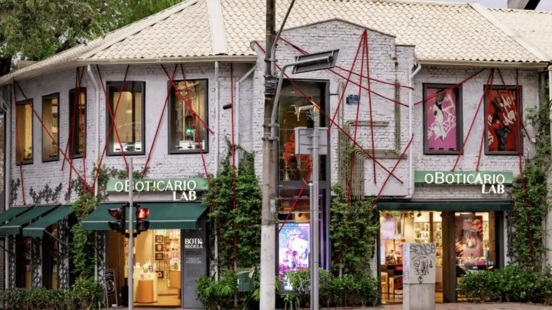 Fachada da loja O Boticário Lab decorada para a colaboração com a Marvel, com teias de aranha vermelhas e pôsteres nas janelas.
