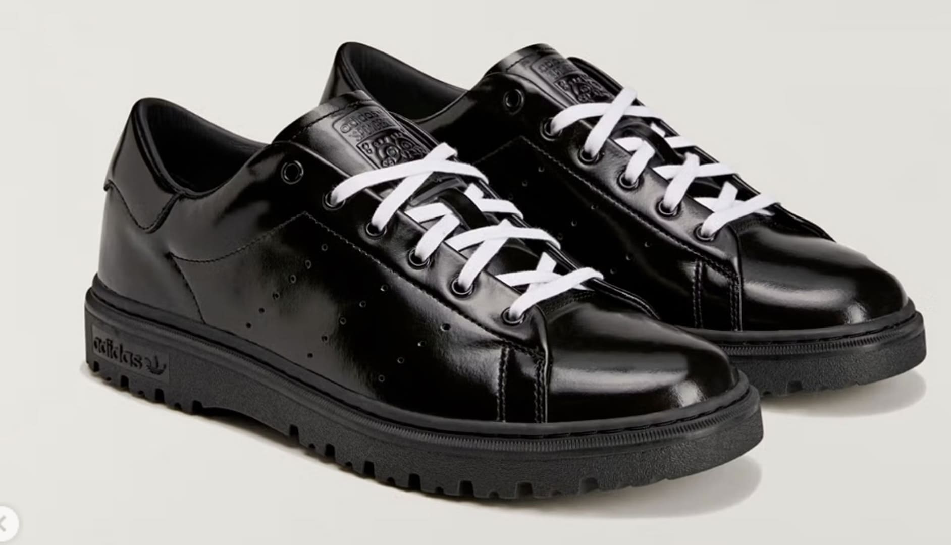 Par de tênis Adidas Stan Smith Freizeit preto brilhante com cadarços brancos, parte da colaboração com Bob Esponja, em um fundo neutro.