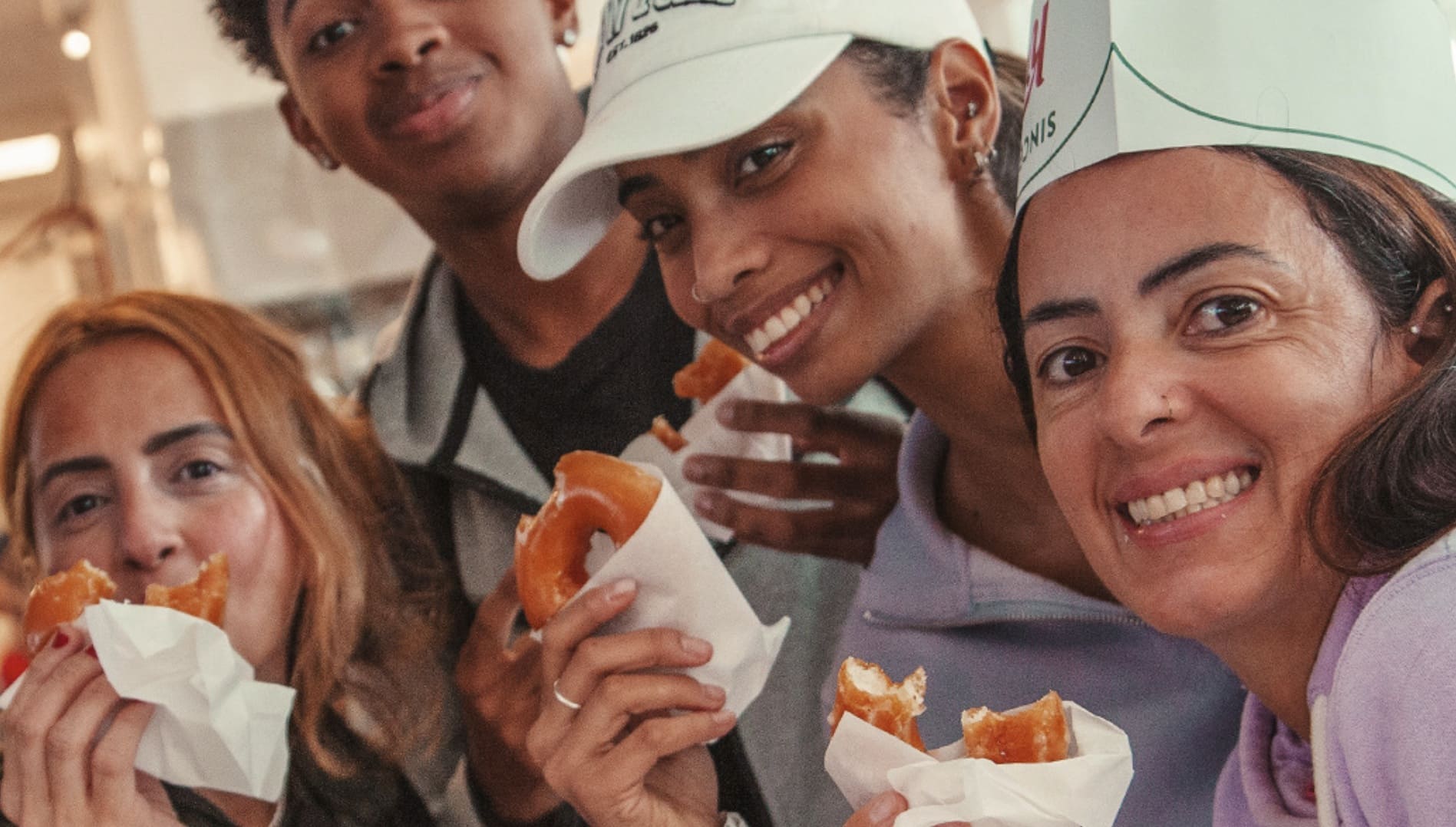 Quatro pessoas sorrindo e comendo donuts Krispy Kreme.
