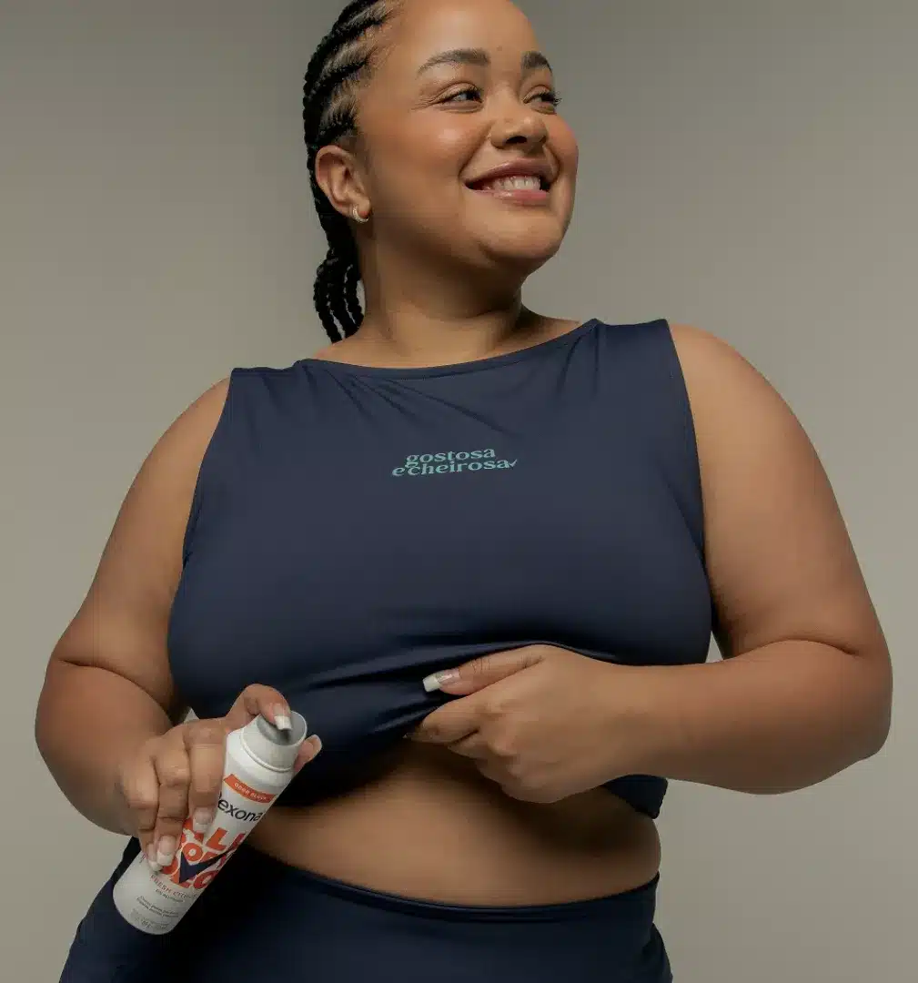 Lela Brandão sorri enquanto segura e aplica um desodorante Rexona.