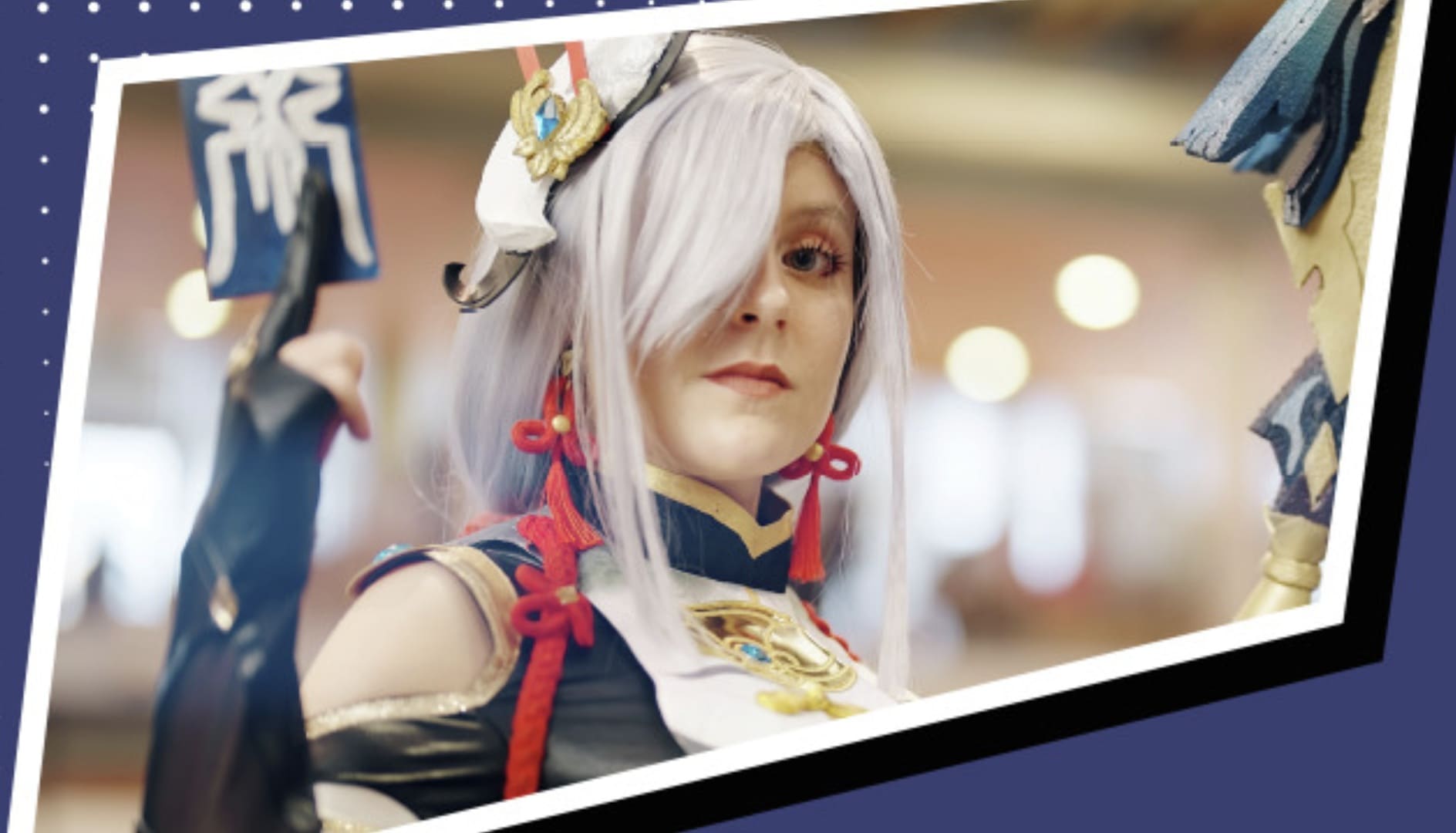 Close-up de uma cosplayer vestida como Shenhe do jogo Genshin Impact, segurando um talismã na mão esquerda.
