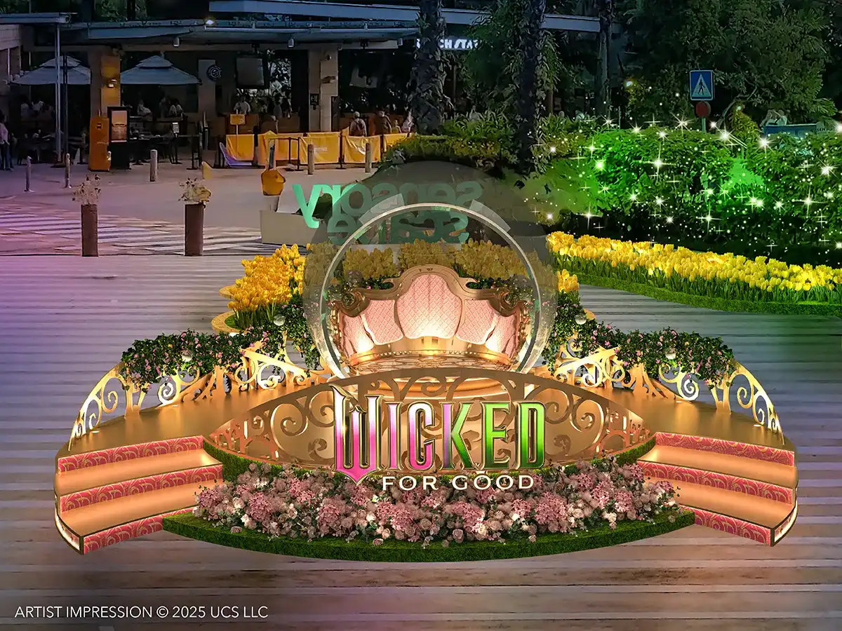 Instalação de palco e trono dourados com a logo "Wicked For Good" em um jardim temático ao ar livre.
