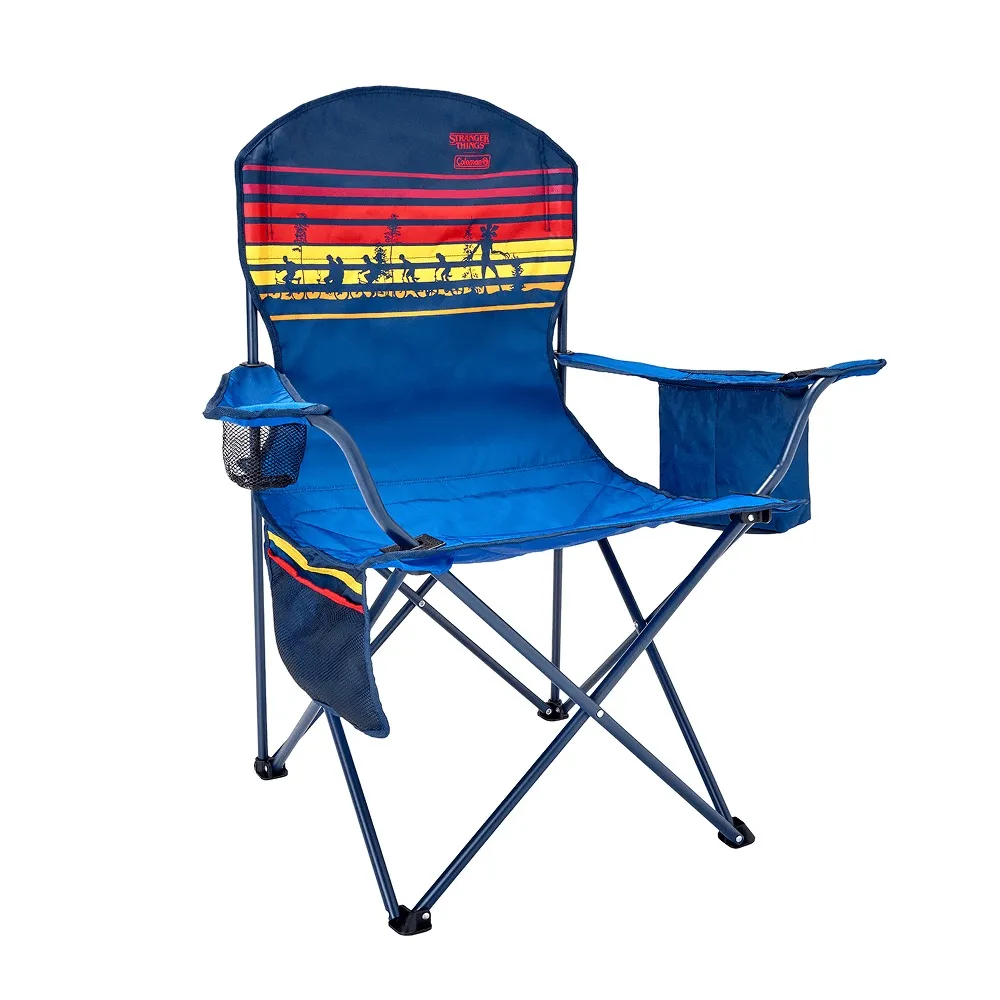 Cadeira de camping dobrável Coleman azul com design de Stranger Things na parte de trás, apresentando silhuetas de personagens caminhando contra listras horizontais vermelhas, amarelas e azuis, e porta-copos.