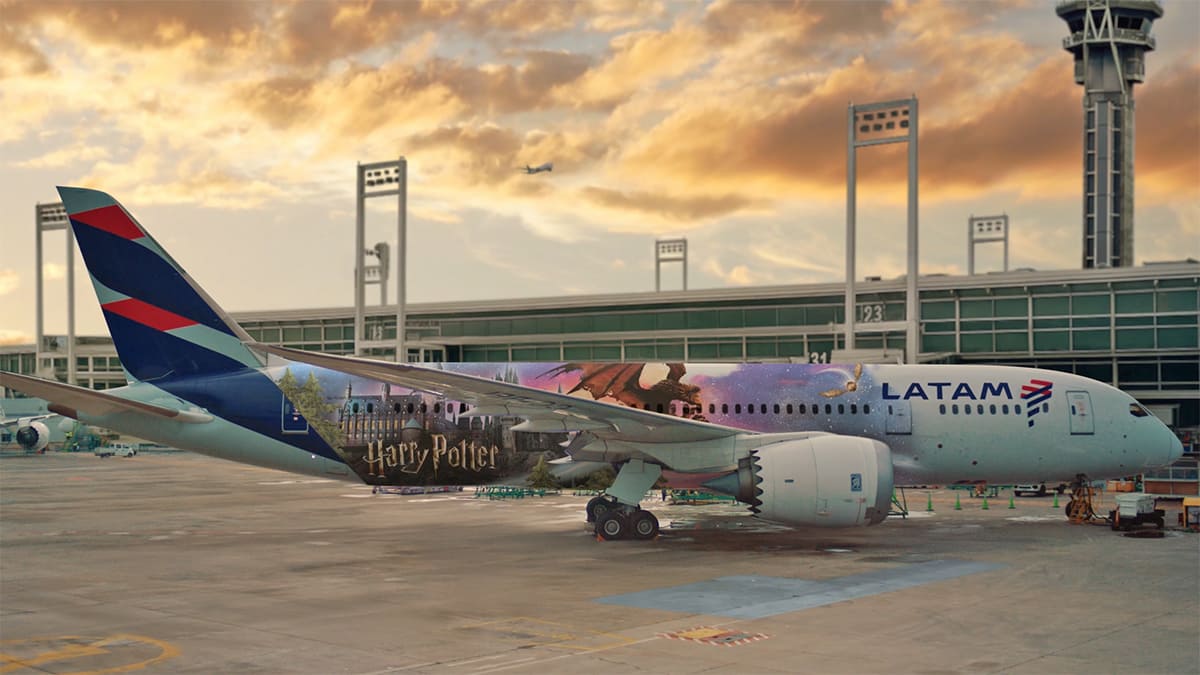 Avião Boeing 787 da LATAM com pintura especial temática de Harry Potter, mostrando Hogwarts e um dragão contra um céu alaranjado, estacionado em um aeroporto.