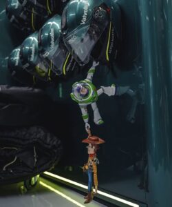 Os bonecos de Woody e Buzz Lightyear pendurados em uma cena de resgate. Buzz está pendurado em um capacete de corrida verde da Aston Martin e segura a mão de Woody, que está pendurado no ar.