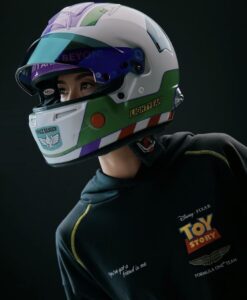 Um capacete de corrida da F1 customizado com as cores e o design de Buzz Lightyear de Toy Story, sendo usado por uma pessoa. A pessoa veste um moletom preto com o logo de Toy Story e o emblema da Aston Martin Formula One Team.