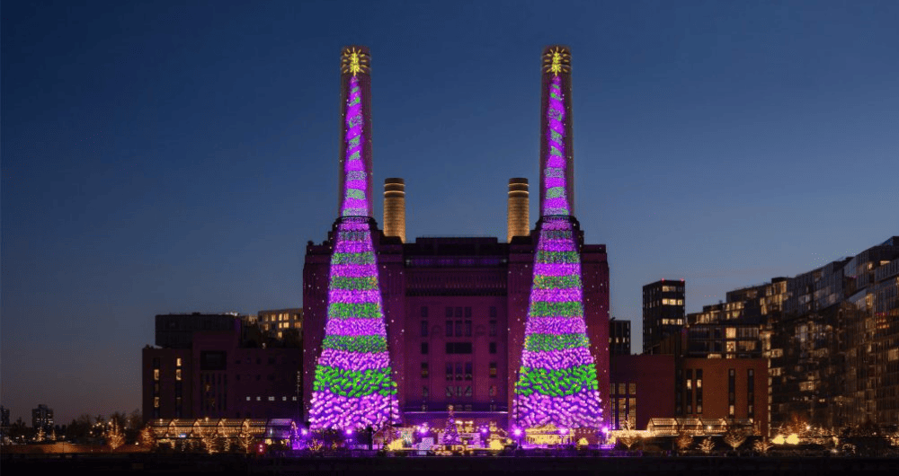 As quatro chaminés da Battersea Power Station exibem árvores de Natal digitais e vibrantes com projeções nas cores roxo, verde e rosa contra o céu noturno azul.