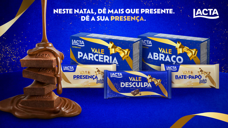 Banner da campanha de Natal da Lacta com a frase "Neste Natal, dê mais que presente. Dê a sua presença.", mostrando chocolates em formatos de "Vale Parceria", "Vale Abraço", "Vale Presença", "Vale Desculpa" e "Vale Bate-Papo", com chocolate derretido e fitas douradas em fundo azul escuro.