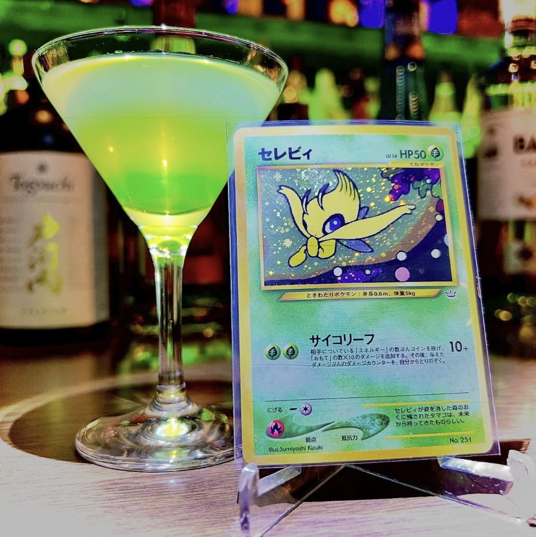 Coquetel verde limão em taça de Martini ao lado de uma carta de Pokémon do Celebi.