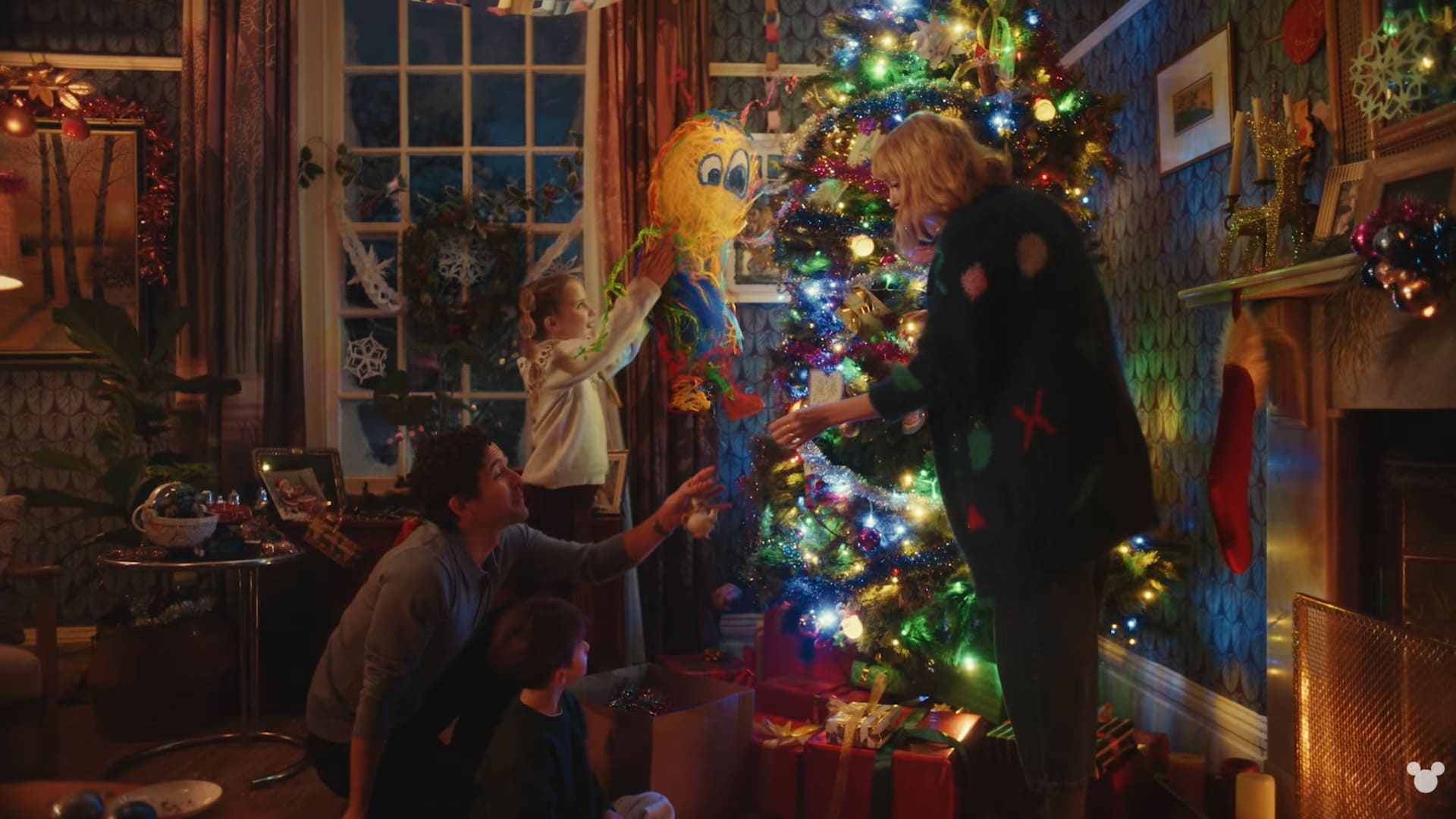 Uma família decora uma árvore de Natal iluminada com uma piñata amarela.